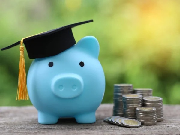 Graduation hat on blue piggy bank with stack of coins money on nature green background, Saving money for education concept