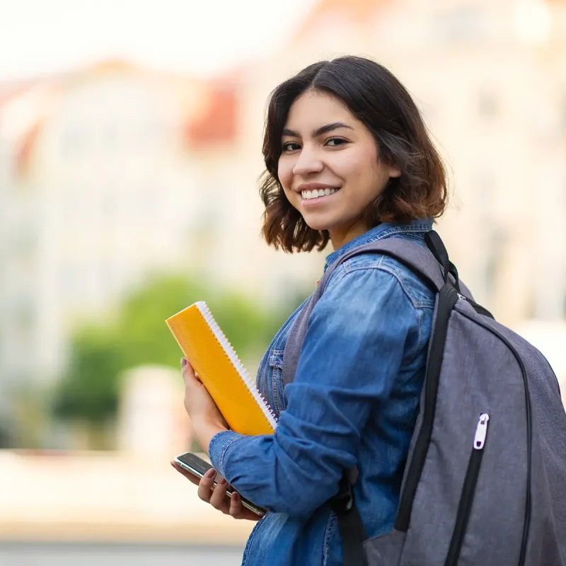 Smiling Young Arab Female Student With Workbooks And Backpack Standing Outdoors, Happy Middle Eastern Millennial Woman Posing Outside At University Campus, Turning At Camera, Copy Space